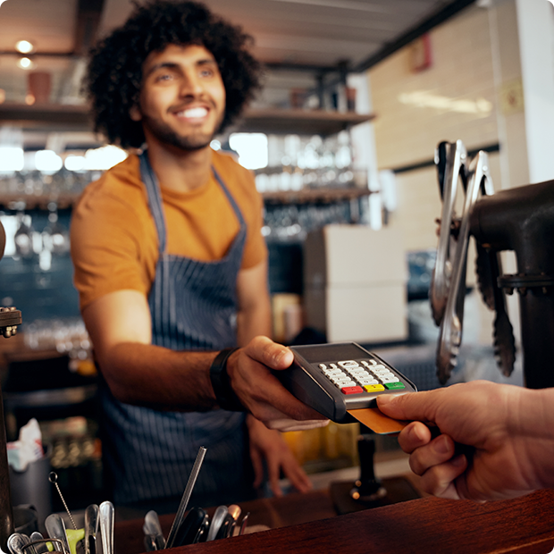 Kellner hält Kreditkartenlesegerät in der Hand, während Kunde Code in modernem Café eingibt